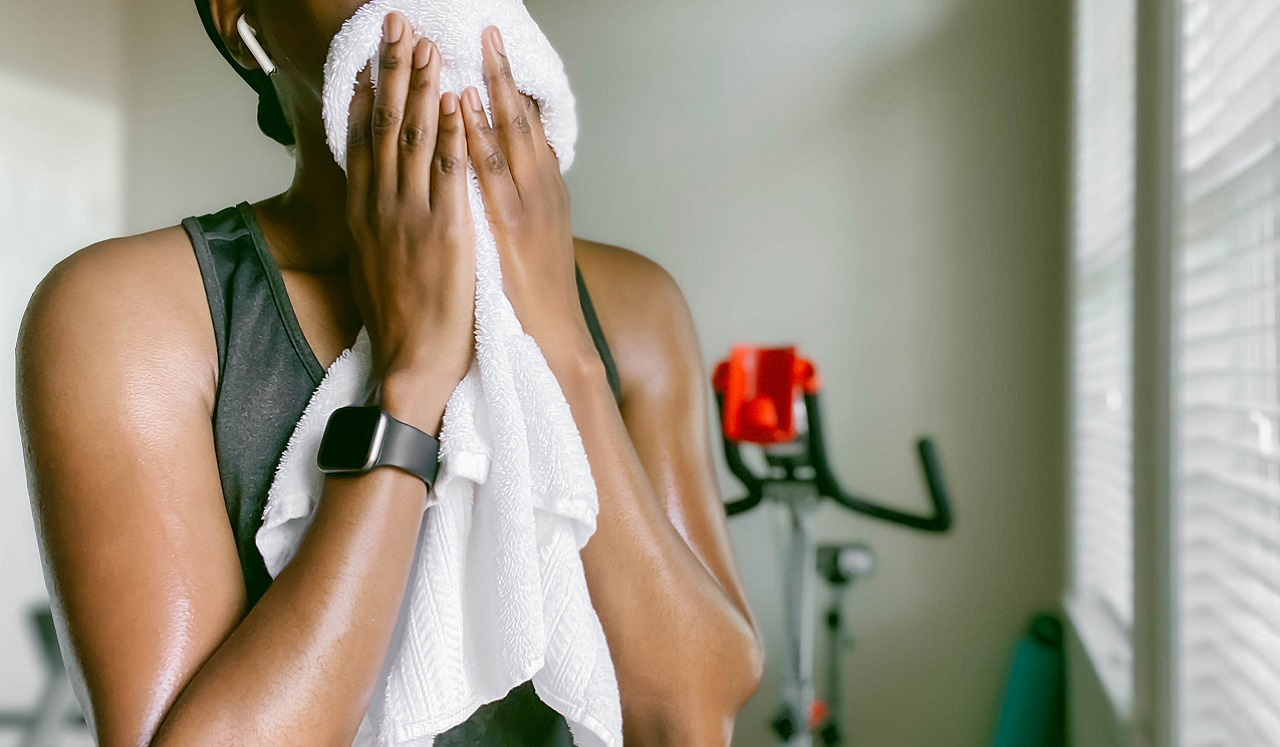 A woman in her home gym holds a towel up to her face, as if wiping away sweat after a workout.