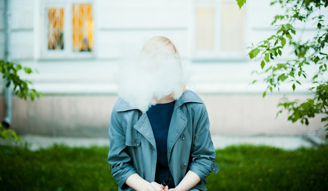 A person blowing out smoke or vapor that is obscuring their face.