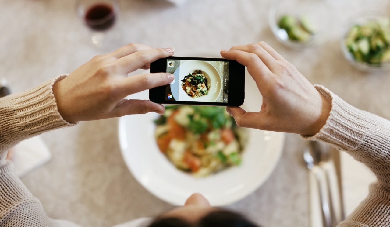 A woman holding a phone and taking photo of food.