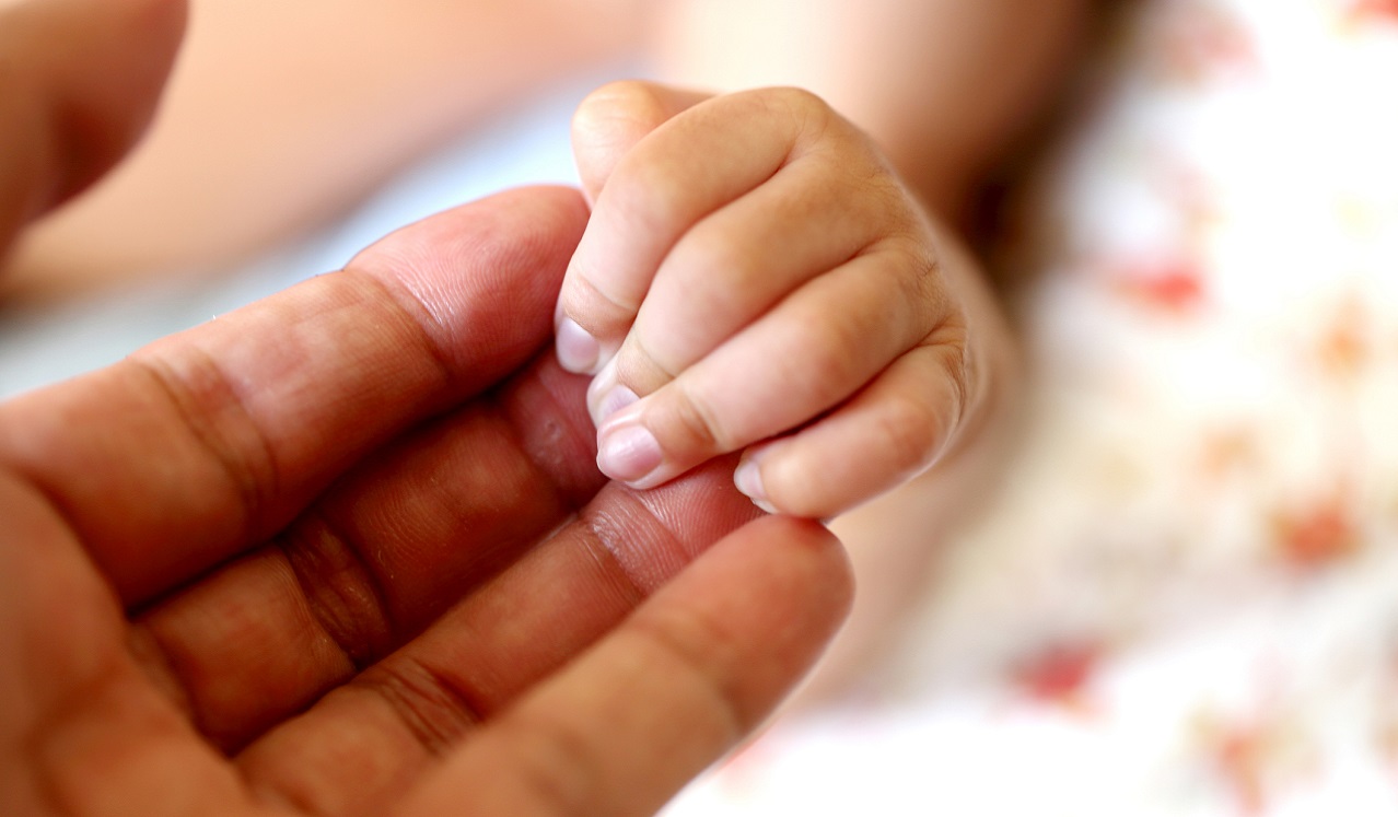 An adult hand holding an infant hand.