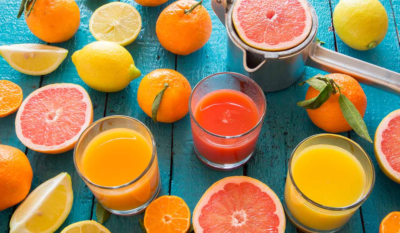 Glasses of juice and surrounded by sliced citrus fruits.