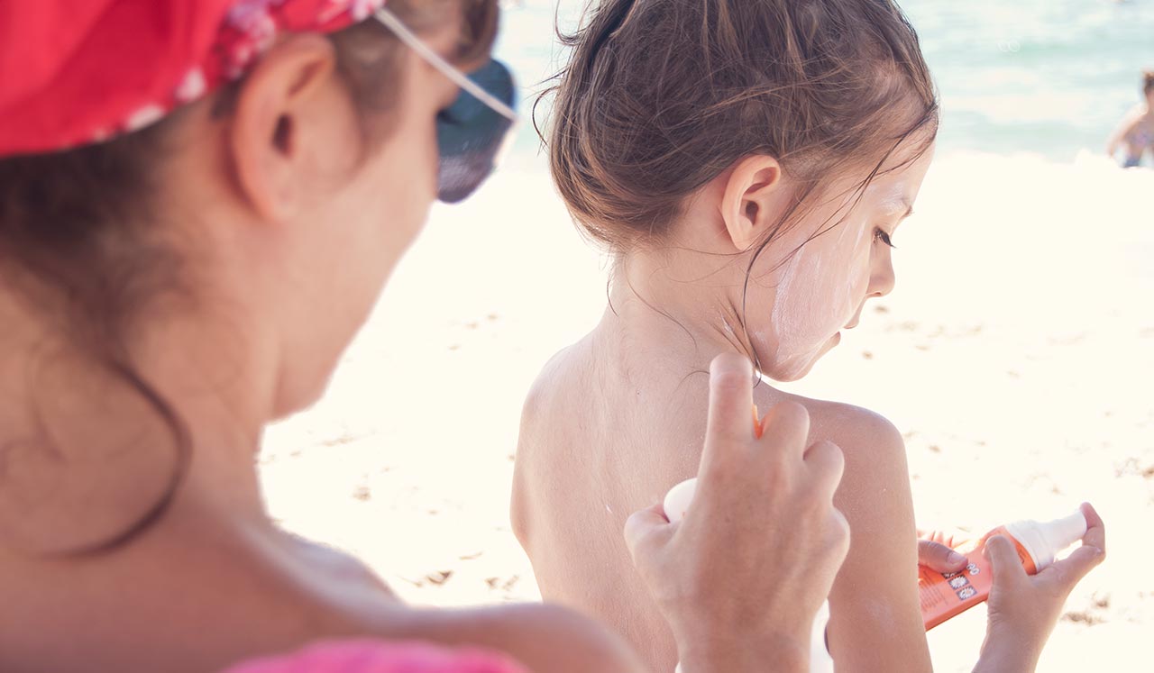 A mom applying sun screen to a child at the beach