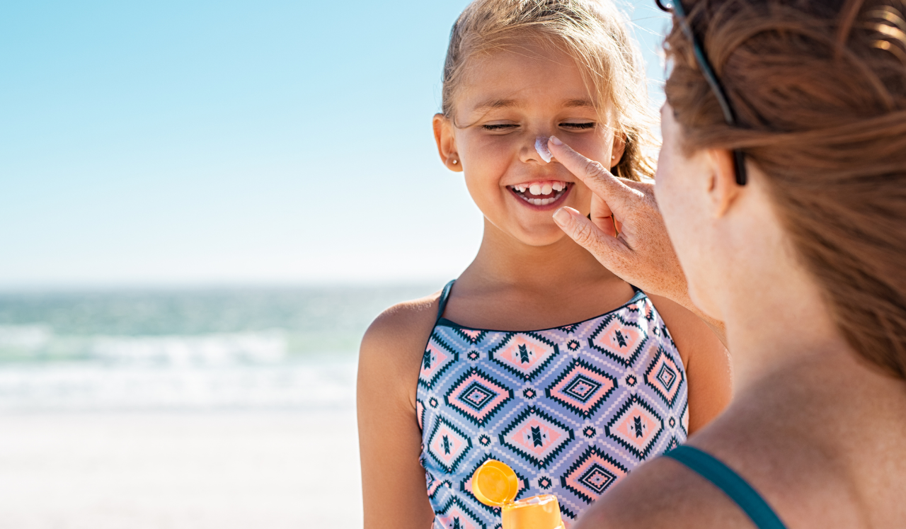 Parent applying sunscreen to child's face at the beach.
