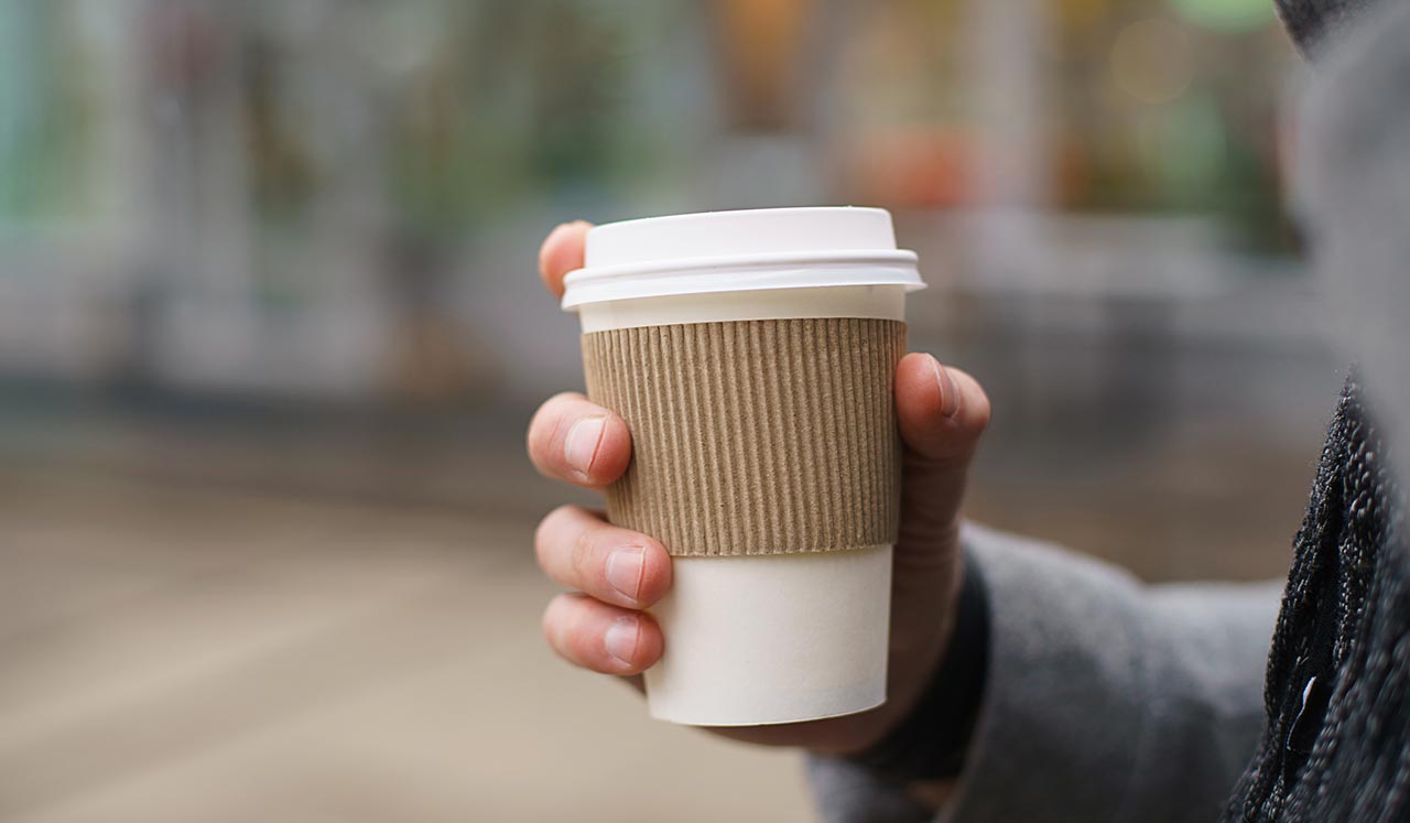 A hand holding a disposable coffee cup.