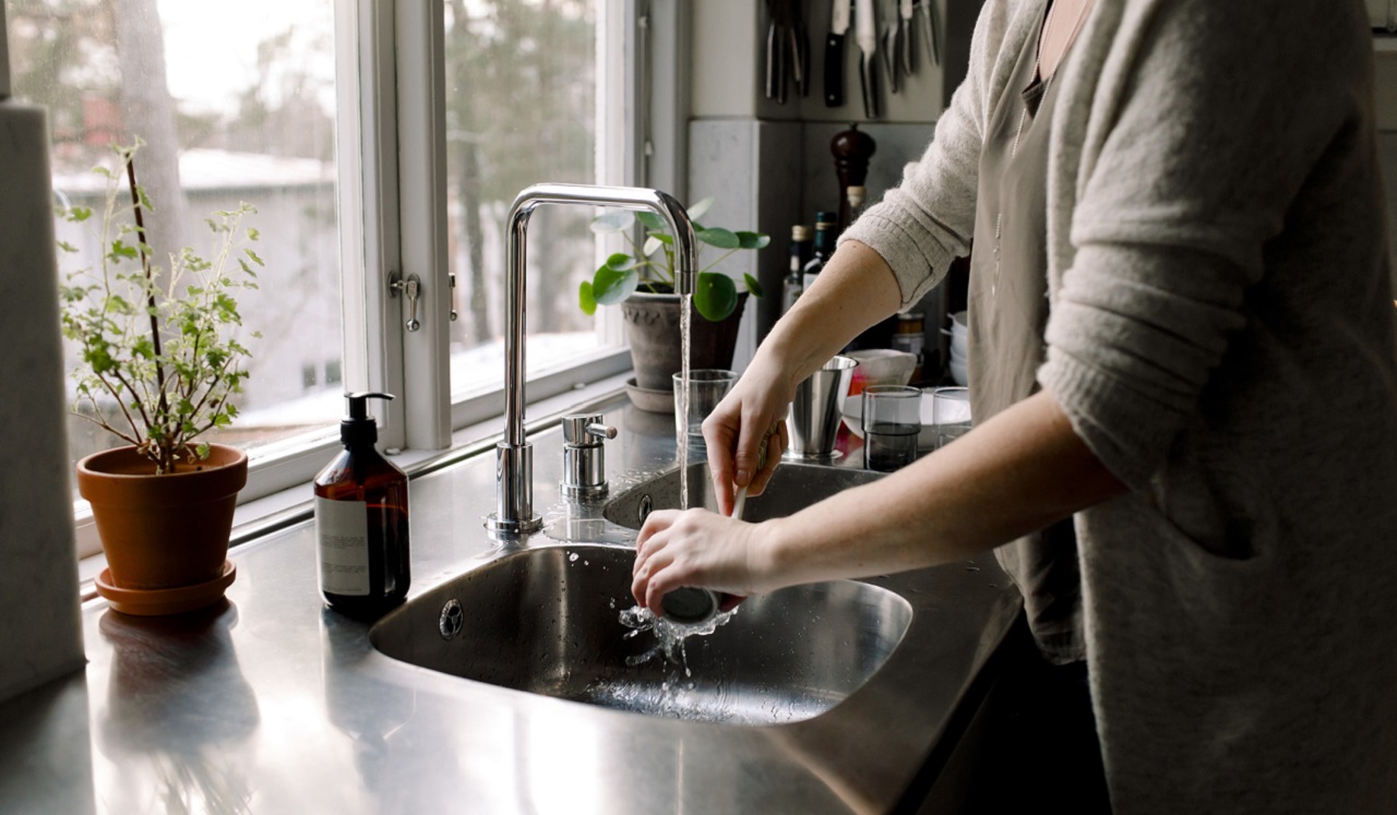 A woman washing dishes at a sink in front of a window.