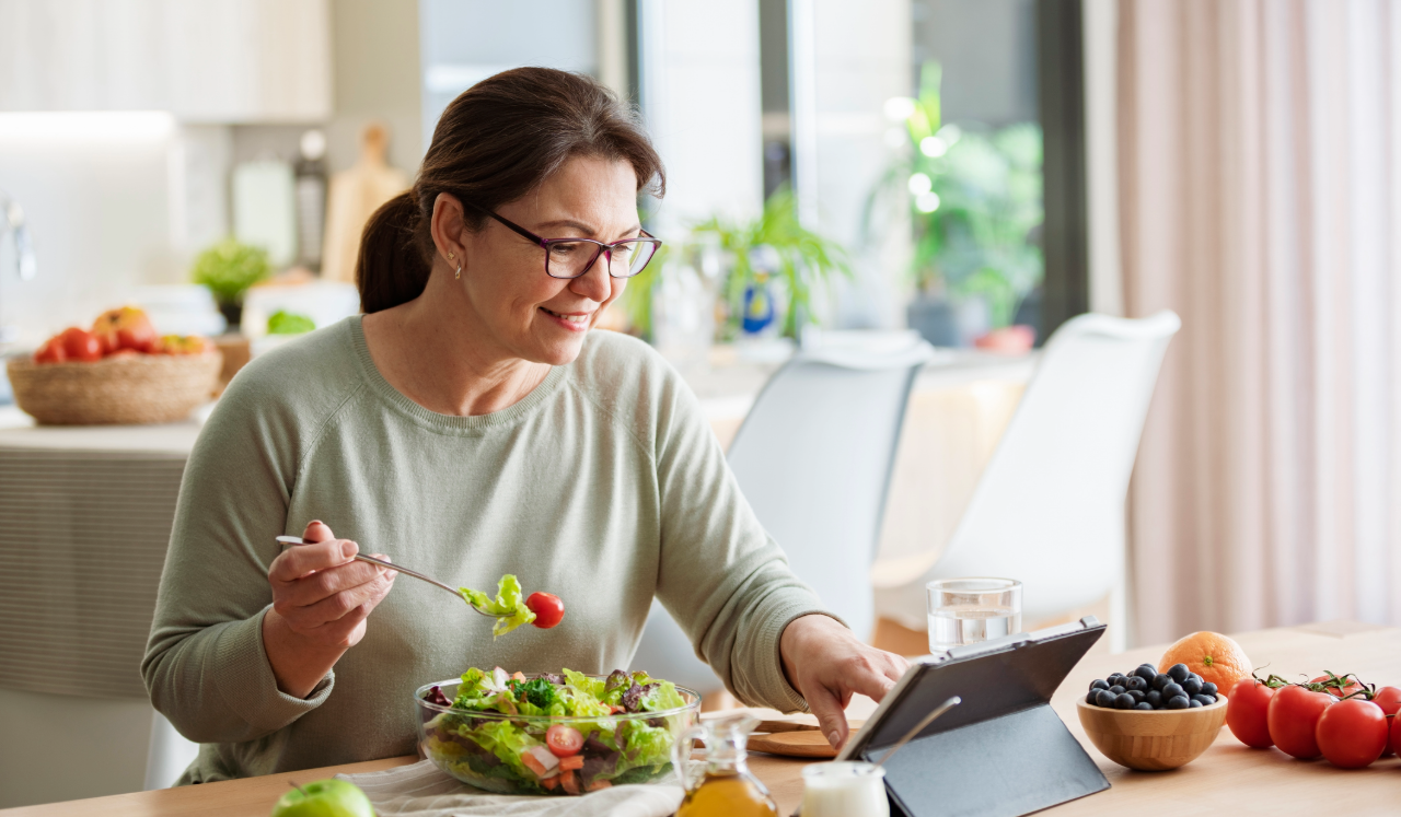 Woman eating salad while scrolling iPad.
