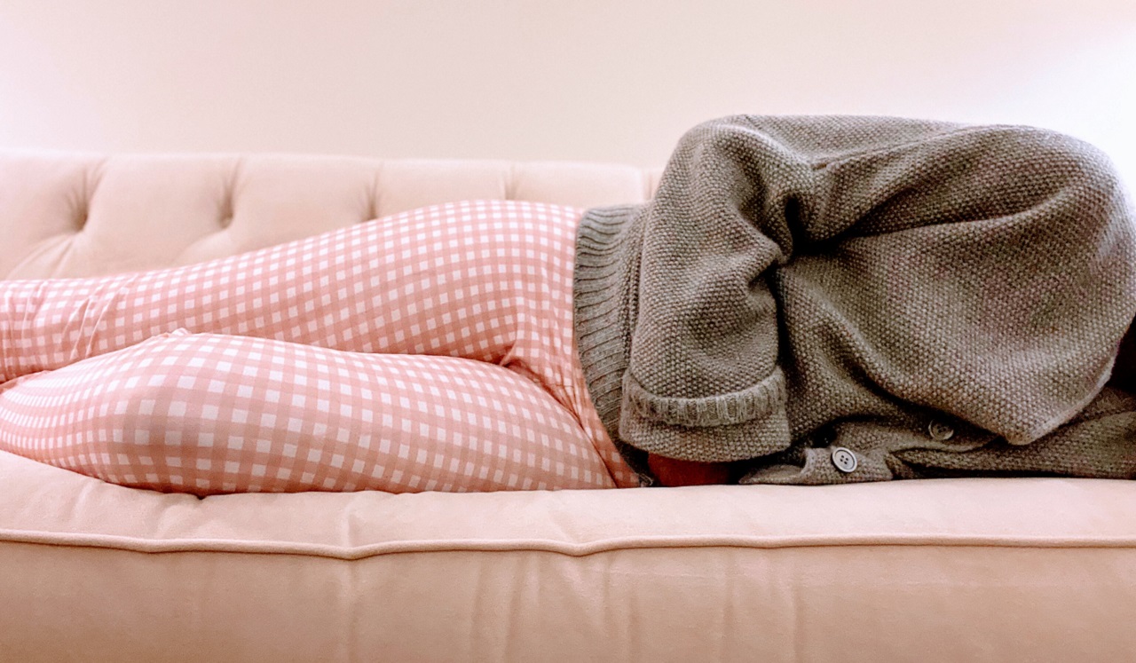 A person in pajamas lying on the couch and holding their stomach.