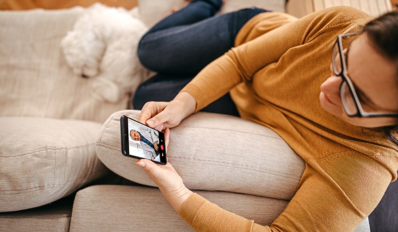 A woman sitting on her couch while on a video call with a physician.