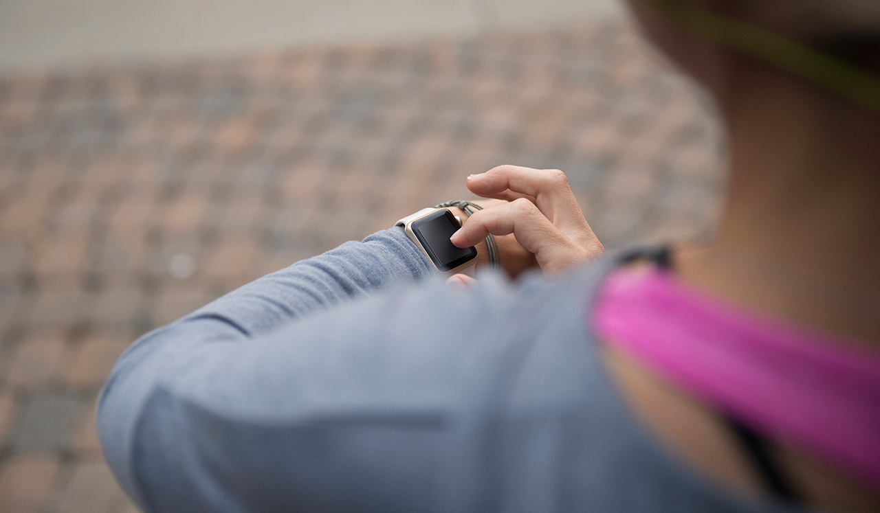 A woman looks down and adjusts her fitness watch.