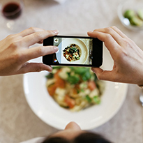 A woman holding a phone and taking photo of food.