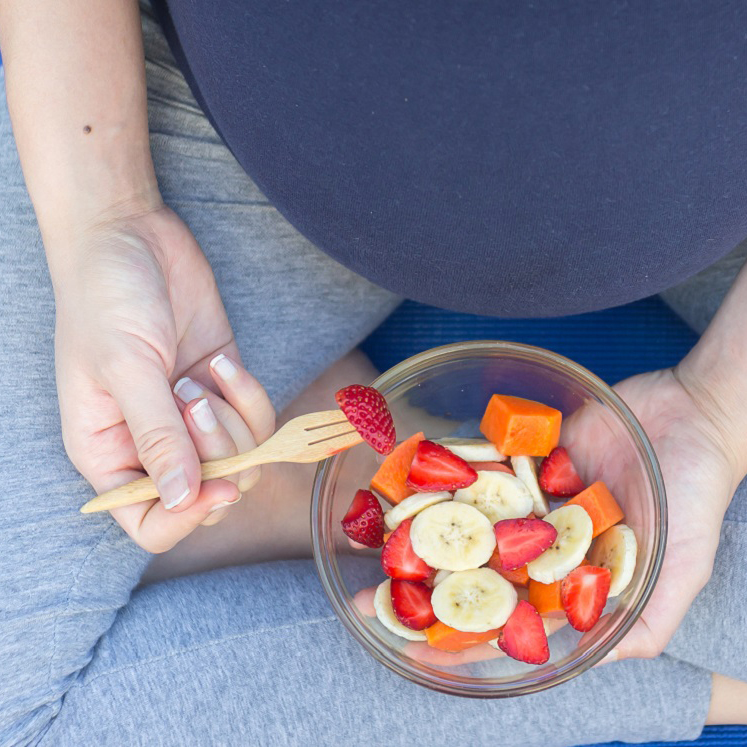 A pregnant woman sitting and eating a bowl of fruit.