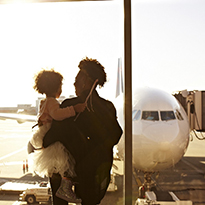 A person holding a child looking at an airplane at the airport.