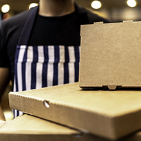 An assortment of take-out food boxes being held by a person donning a striped apron.