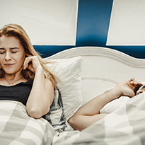 A woman holds her ears as her husband snores beside her.