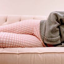 A person in pajamas lying on the couch and holding their stomach.