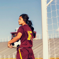 A teenage girl in a sports uniform holding a soccer ball.