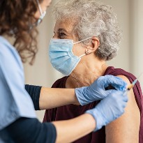 An elderly woman is receiving a shot from a medical professional.