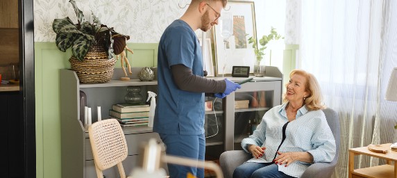 A woman is supported by a caregiver in her home. 