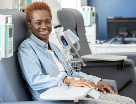 A woman smiles from a comfortable chair while receiving IV fluids.