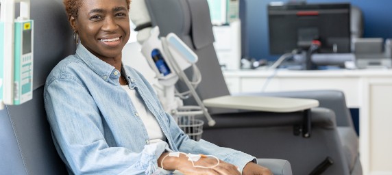A woman smiles from a comfortable chair while receiving IV fluids.