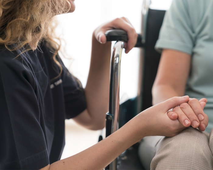 A woman tenderly holds the hand of a home care patient.