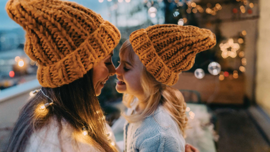 A woman and her daughter touch noses affectionately, wearing matching winter hats.