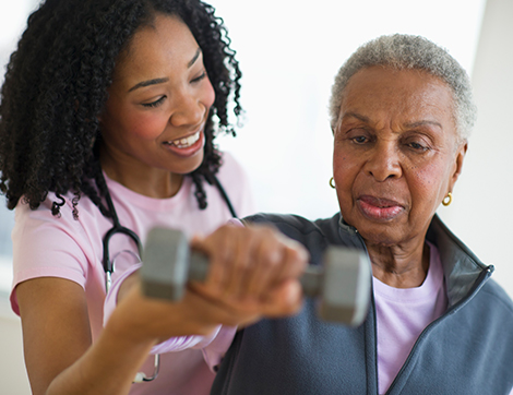 A home health professional helps a woman while lifting a hand weight.