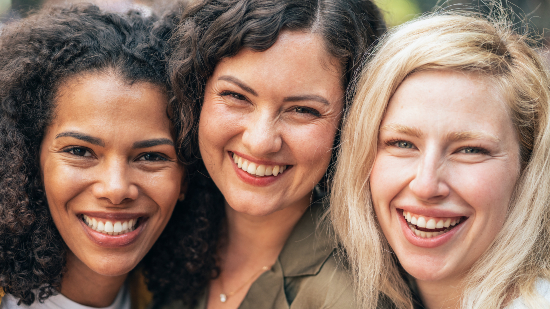 Three friends smile and laugh for a close up photo together.