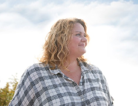 A woman in a plaid shirt smiles as she looks off into the distance of the great outdoors.