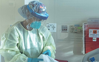 A healthcare worker in gloves, gown and mask in a patient room.