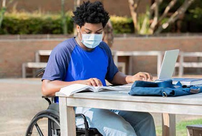 A man in a wheel chair studying outdoors with books and laptop