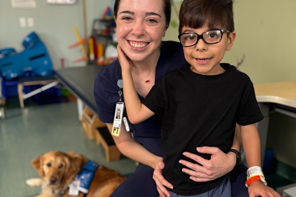 TIRR Memorial Hermann pediatric patient, service dog Annie, and therapist smile for a photo.