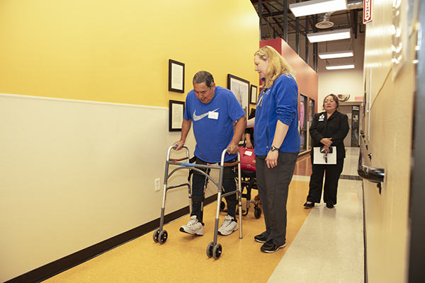 A man uses assistive equipment to walk down the hall.