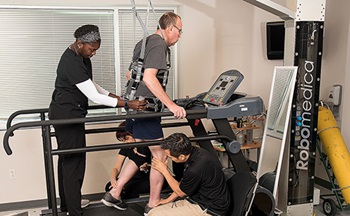 Therapists help patient walk on assistive equipment