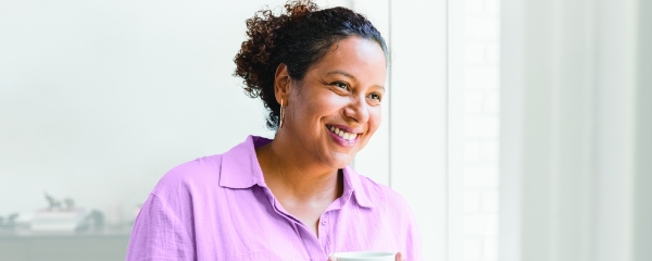 A woman smiles while holding a cup of coffee.