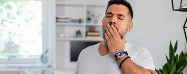 A man covers his mouth while yawning.