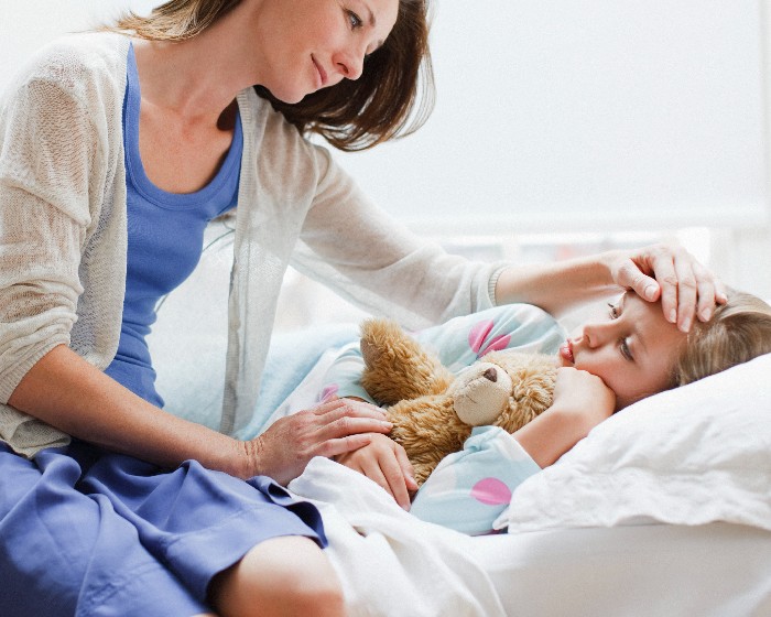 A woman sits at her daughters bedside and caresses her forehead.