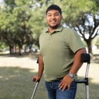 A TIRR Memorial Hermann patient smiles while standing with assistive devices.